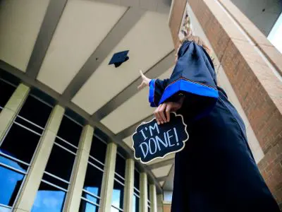a graduating female student tossing her cap and tassel into the air.