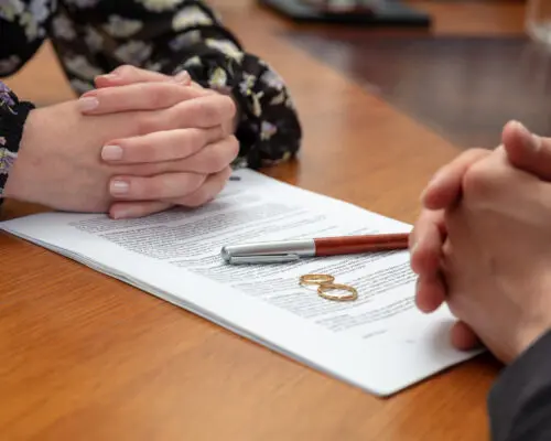 Signing a divorce, marriage dissolution documents and agreement. Wife and husband hands, wedding rings and legal papers for signature on a wooden table, lawyer office