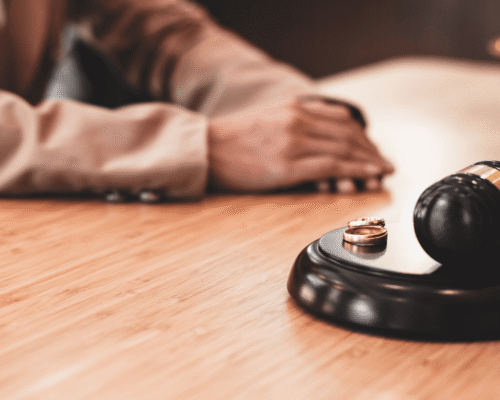 Judge’s gavel beside two wedding rings on a wooden desk with a person seated in the background, symbolizing how long can a divorce take in Pennsylvania. The image reflects divorce in Pennsylvania, contested divorce in Pennsylvania, no-fault divorce in Pennsylvania, Pennsylvania divorce timeline, property division, alimony in Pennsylvania, and child custody in Pennsylvania.